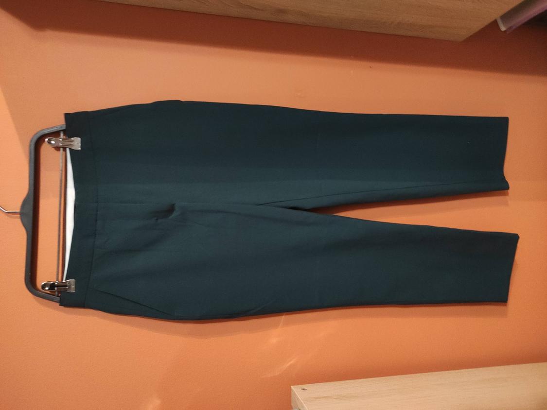 Dark trousers hanging on a hanger against an orange wall. The image depicts a simple, modern style.