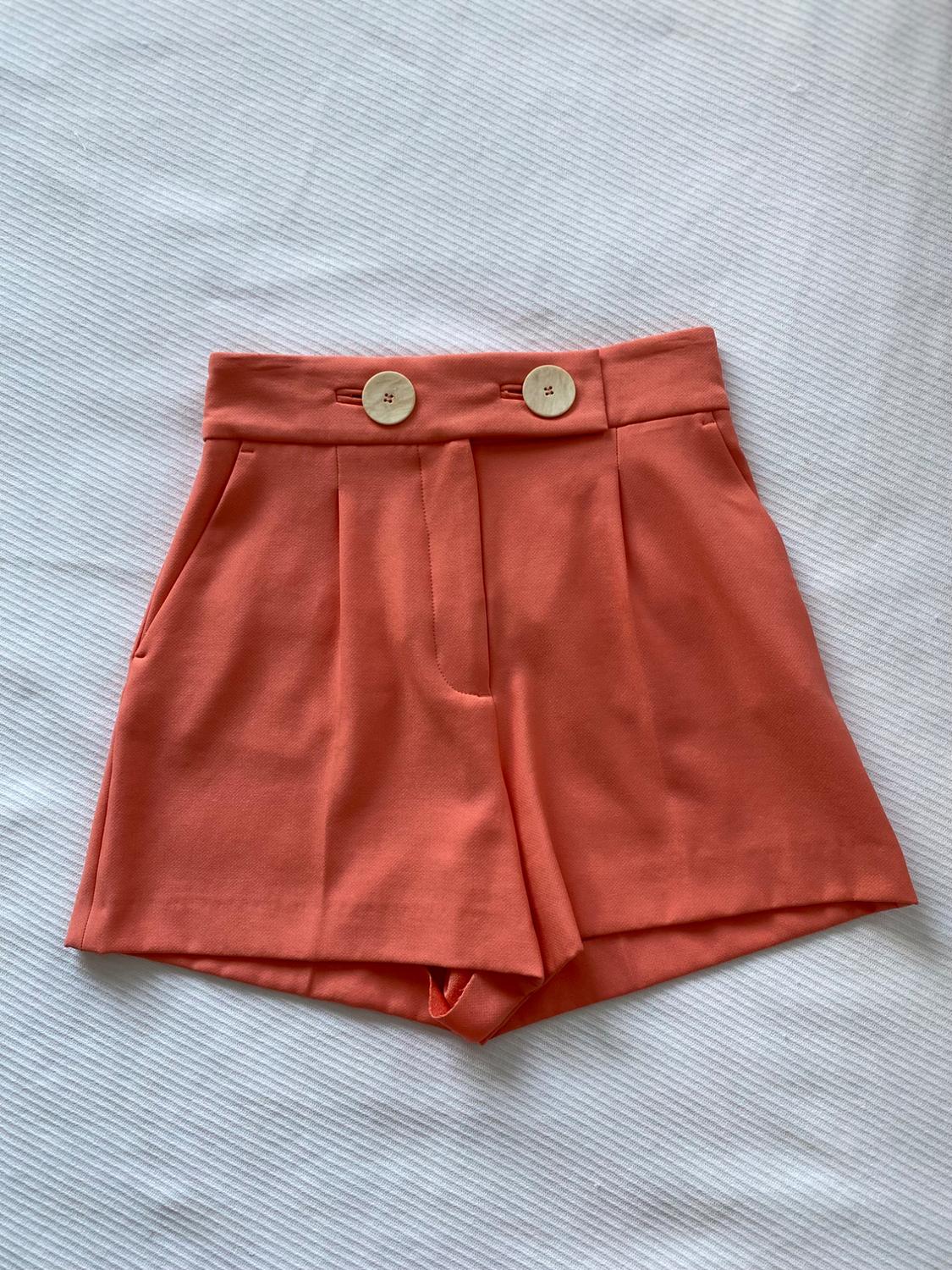 Orange shorts with large buttons at the waist, on a textured white background.