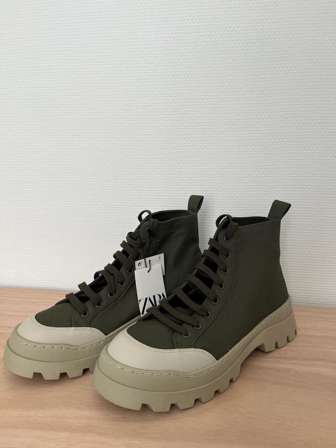 Olive green high-top trainers with a cleated sole and beige toe cap on a wooden surface. Label with the text ZARA.