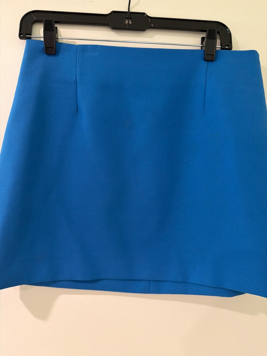 Blue mini skirt with dart detail, hanging on a black hanger against a light-coloured wall.