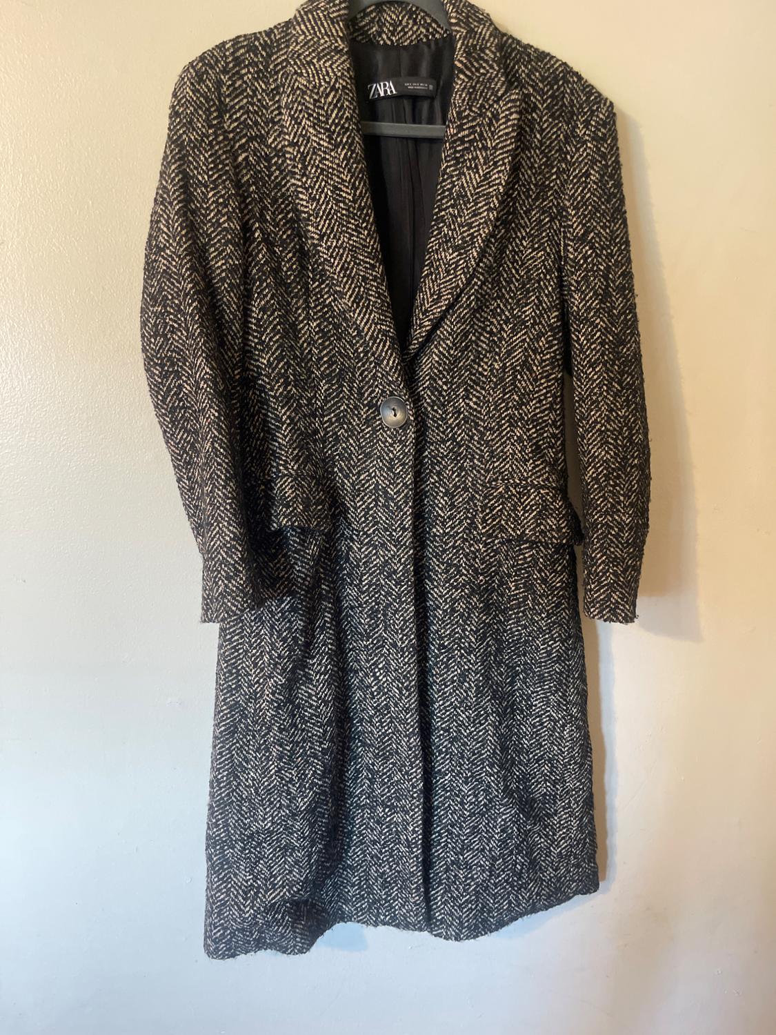 Long wool coat with a black and white herringbone pattern, hanging on a hanger. Visible brand label.