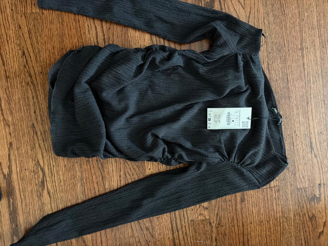 Long-sleeve manga top in dark gray with a ruched texture, spread out on a wooden floor, with a price tag indicating size L.
