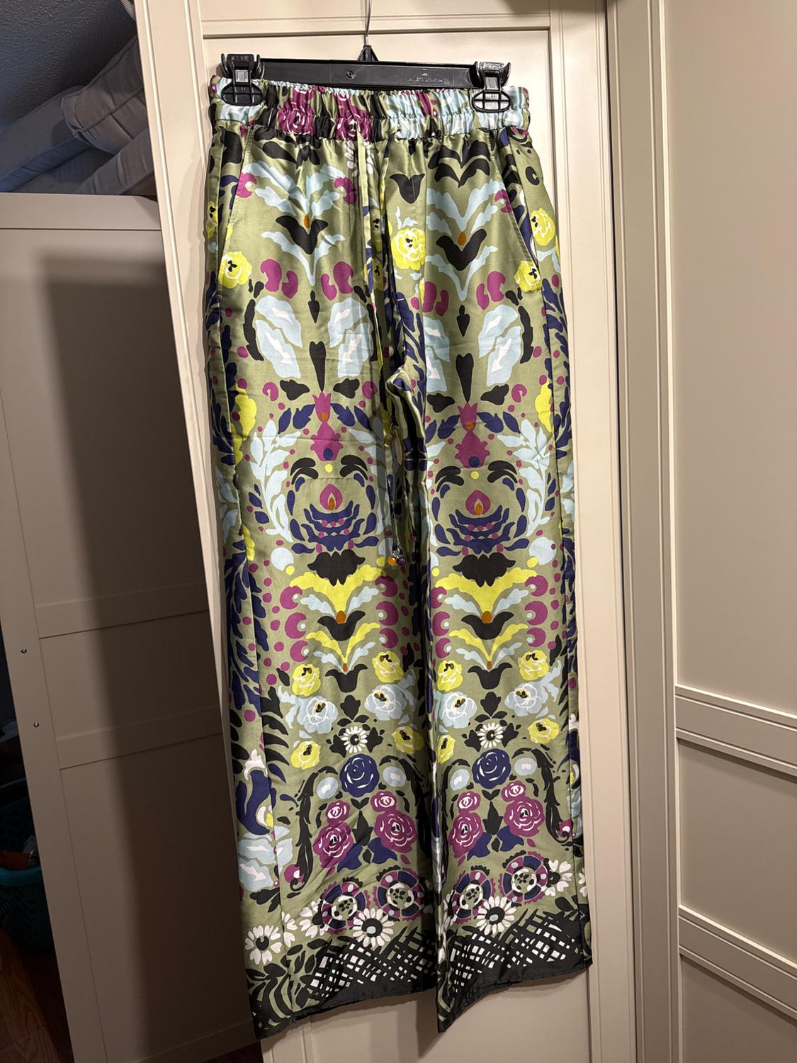 Pants hanging with colorful floral print in green, purple, and yellow tones, on a beige background in a closet.