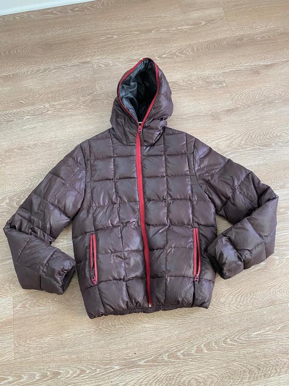 Brown padded jacket with a hood and red zippers, placed on a light wood floor.