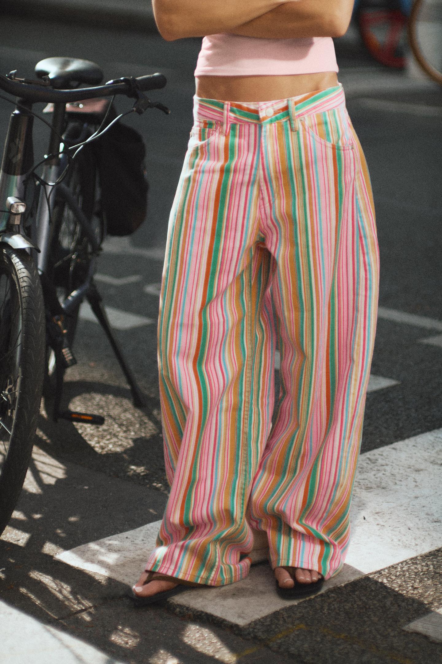 Medium shot of long, baggy, multicolored striped pants. Mid-rise design with a front button, belt loops, and side pockets.