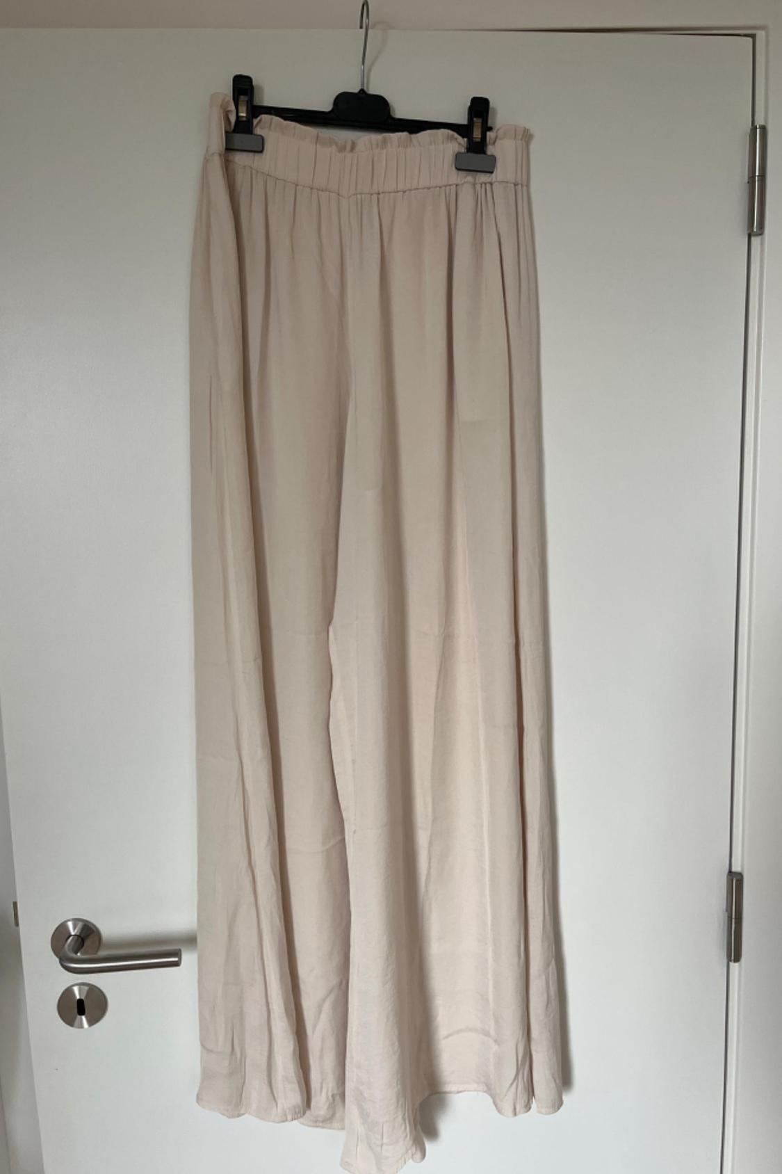 Front view of long beige trousers with an elasticated waistband and a wide cut.