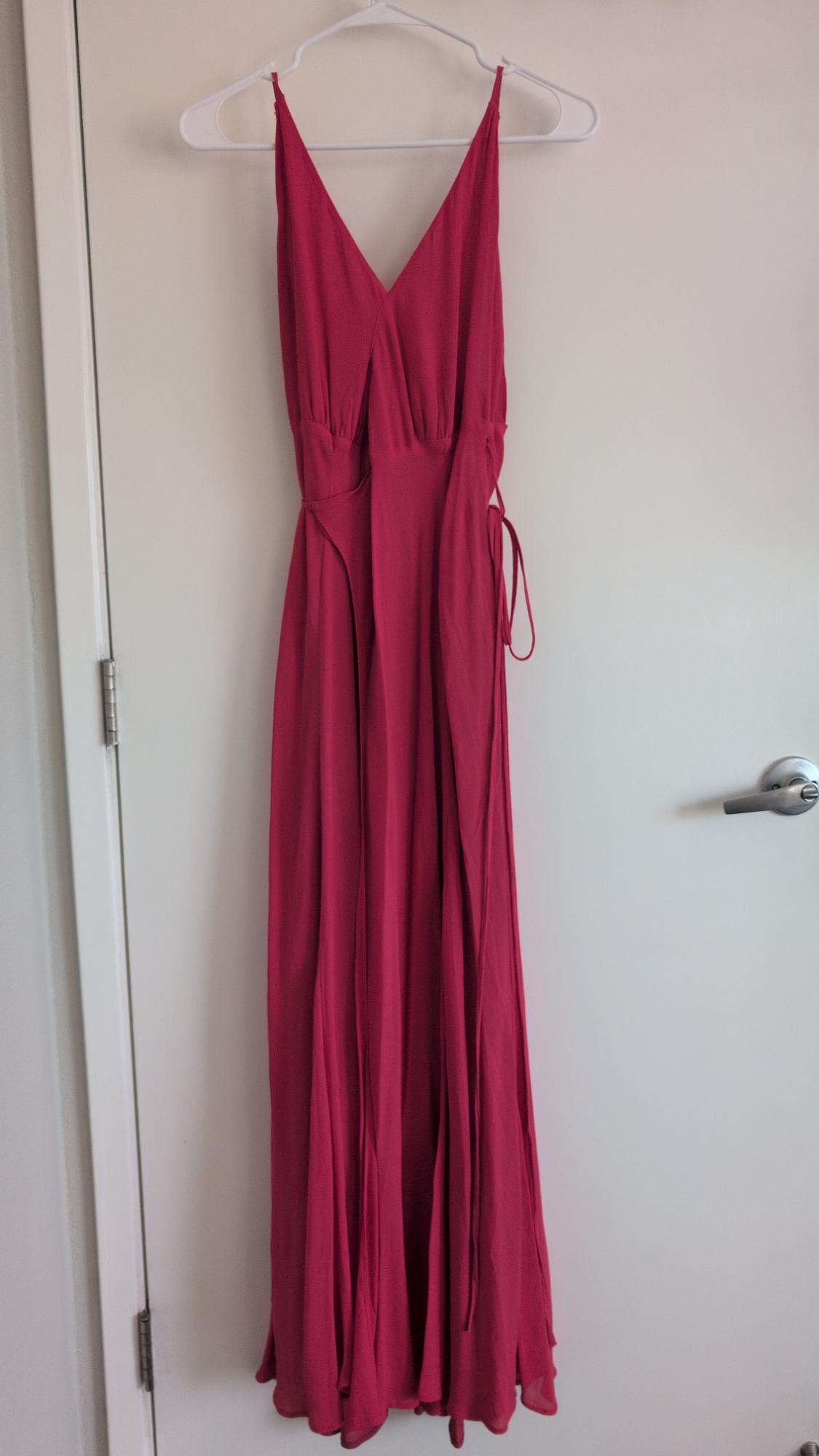 Fuchsia maxi dress with a V-neck, hanging on a white hanger over a white door.