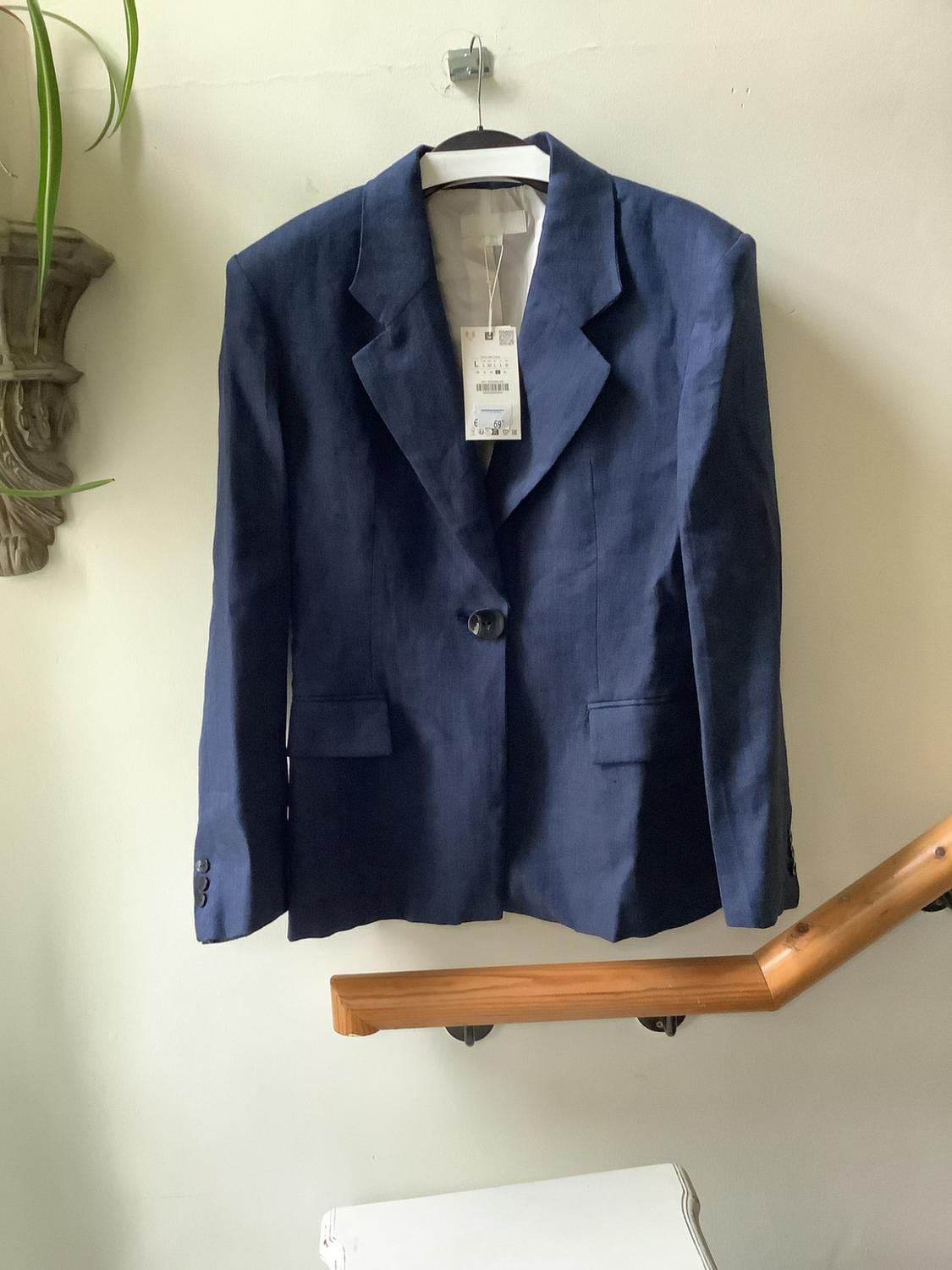 Navy blazer with labels hanging on a coat hanger against a white wall. Below it is a wooden handrail.
