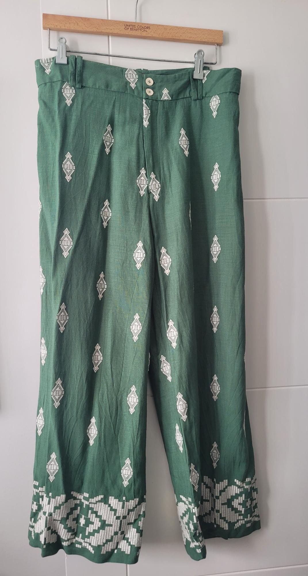 Green trousers with a white geometric print, hanging on a wooden hanger with the text "United Colors of Benetton".