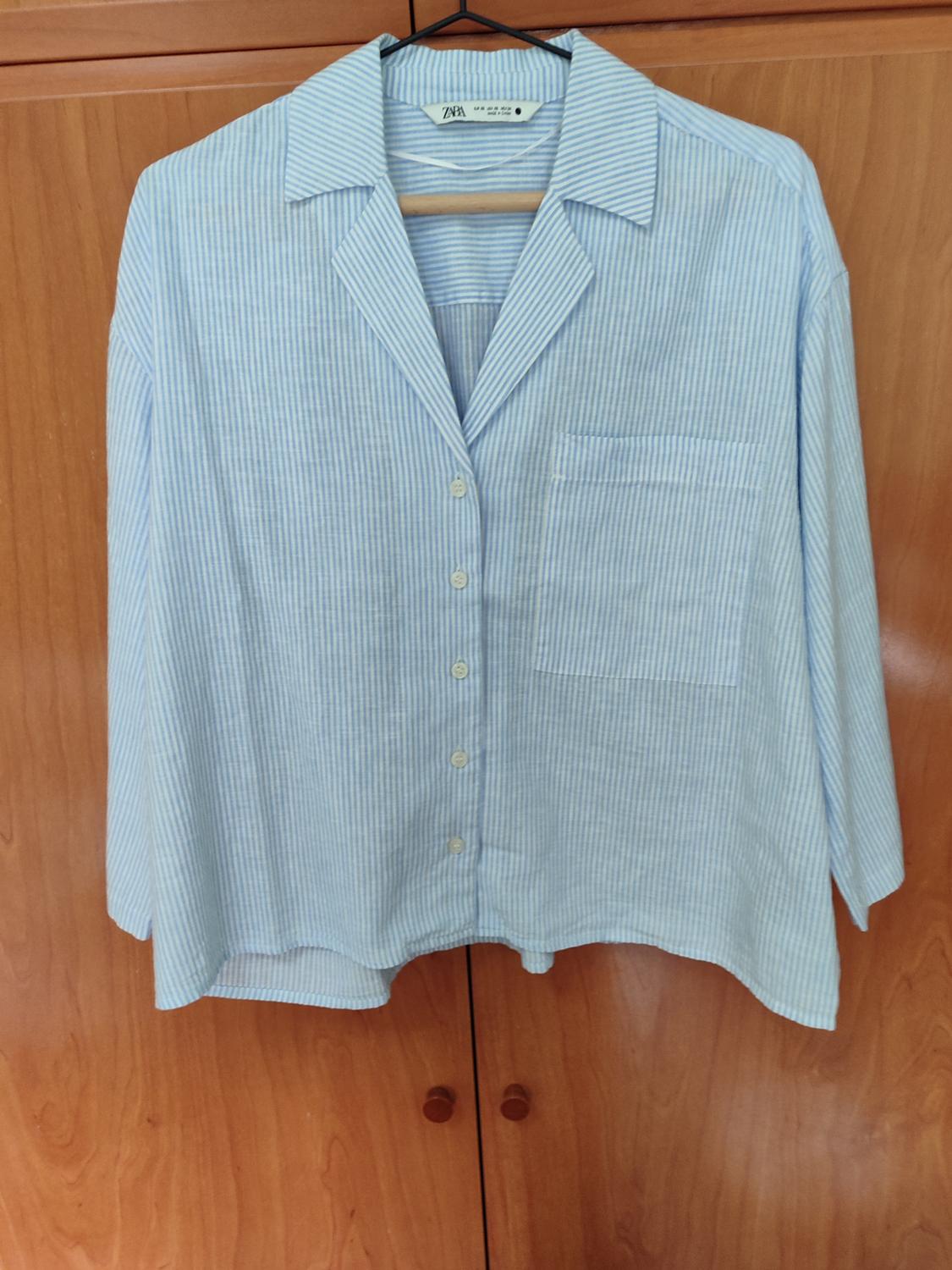 Blue and white striped shirt hanging on a hanger above a wooden wardrobe. Label visible on the neck.