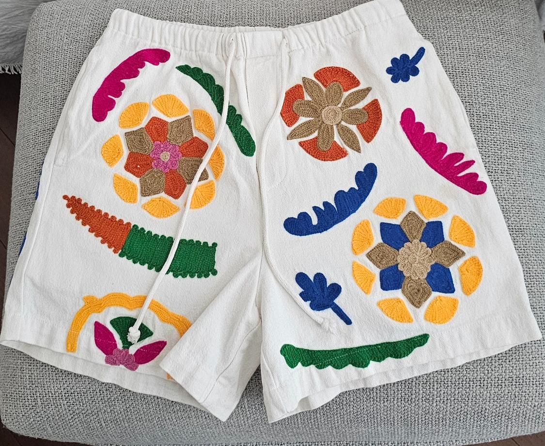 White shorts with colourful floral and abstract embossed motifs. Elasticated waistband with drawstring, on a grey surface.