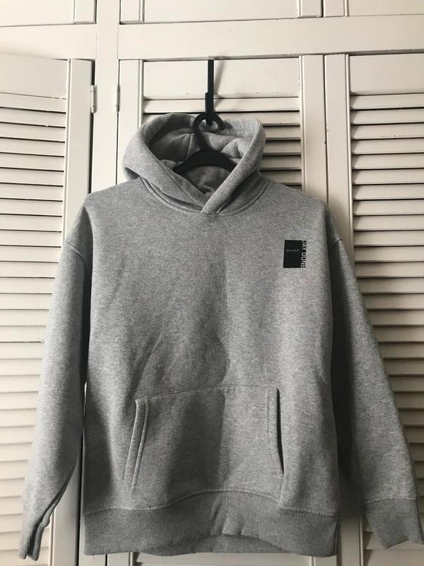 Grey hooded sweatshirt hanging on a black coat hanger in front of white wardrobe doors. Visible text: "AND OUTLINE".