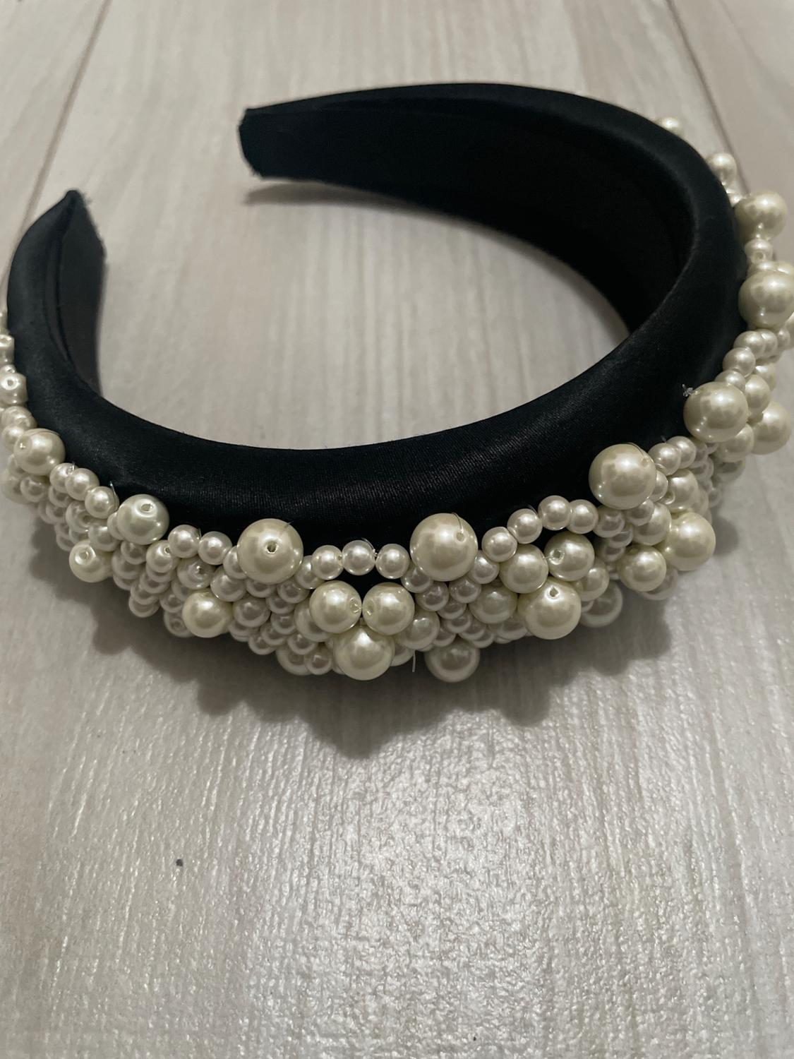 Black headband with white pearls of different sizes on a light wooden surface.