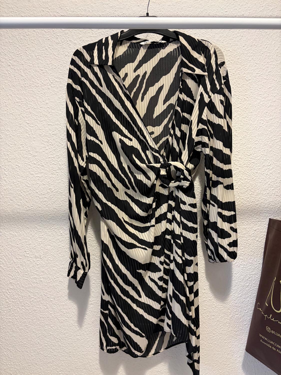 Black and white zebra print long-sleeved dress, hanging on a hanger against a white wall background.