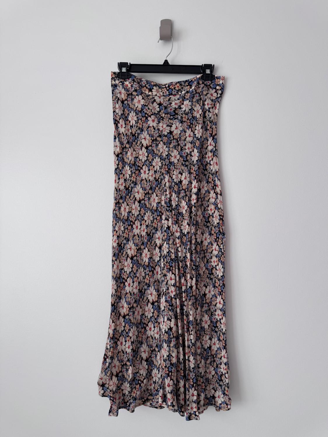 Long dress with a floral print in shades of blue, white, and pink, hanging on a black hanger against a white wall.