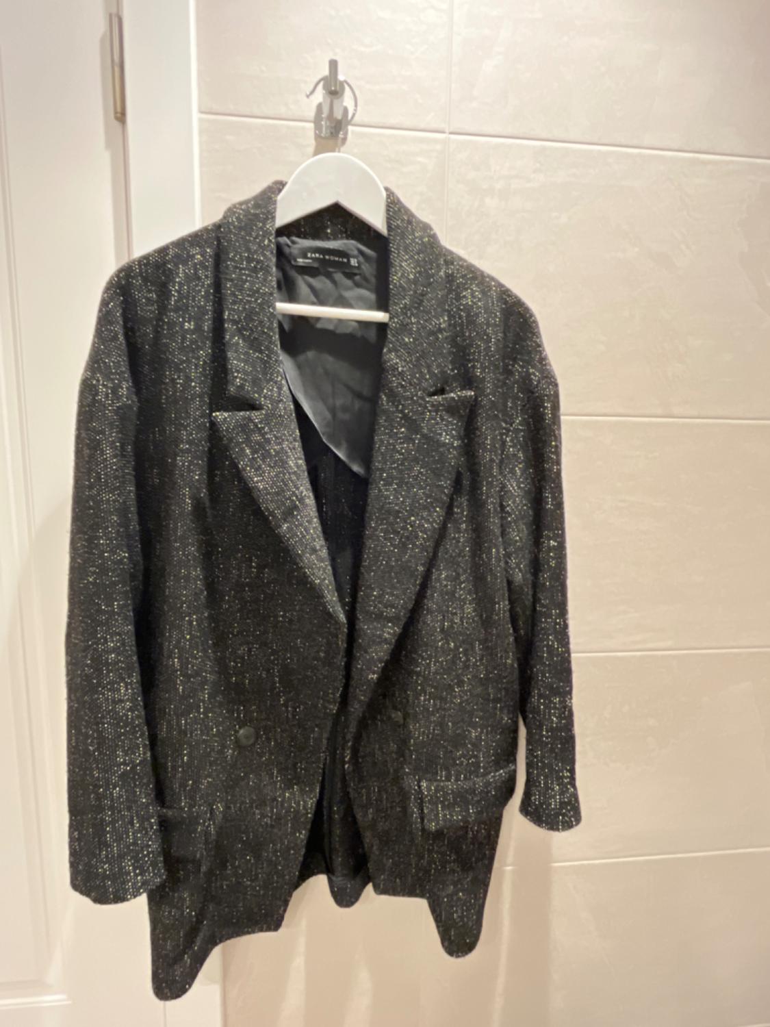 Front view of a black shiny jacket with lapels, front flap pockets.