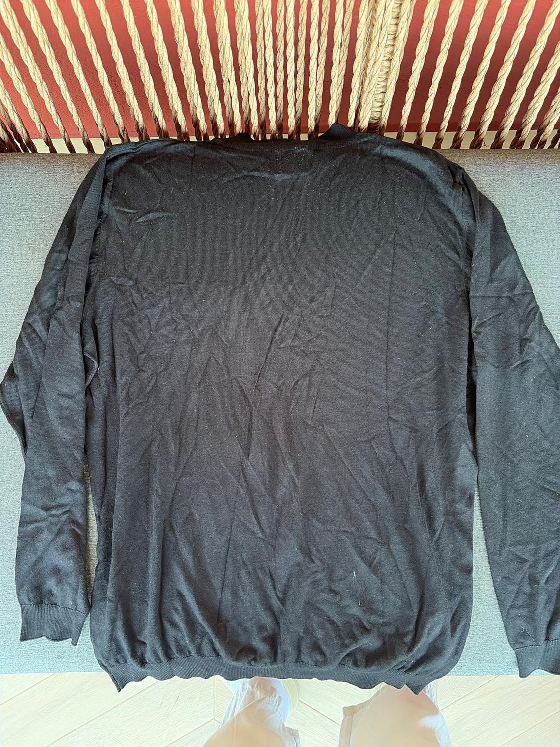 Wrinkled black jumper spread over a grey sofa, with a background of ropes and a red wall. Bottom of trousers and shoes visible.