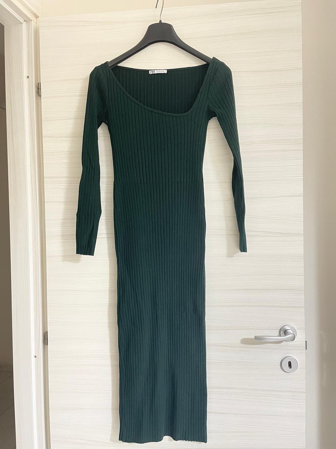 Dark green ribbed knit maxi dress with long sleeves, hanging on a black hanger over a white door.