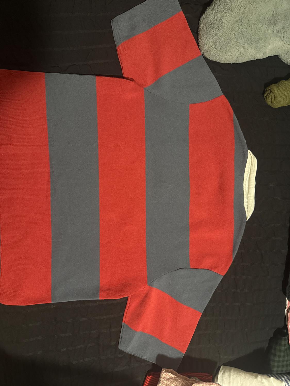Short-sleeved polo shirt with red and gray horizontal stripes and a white collar, on a dark textured background in a relaxed composition.