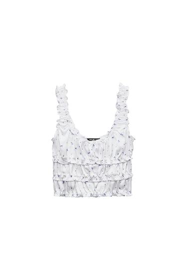 White cropped top with a blue floral print, gathered straps, and horizontal ruffles, photographed on a white background.