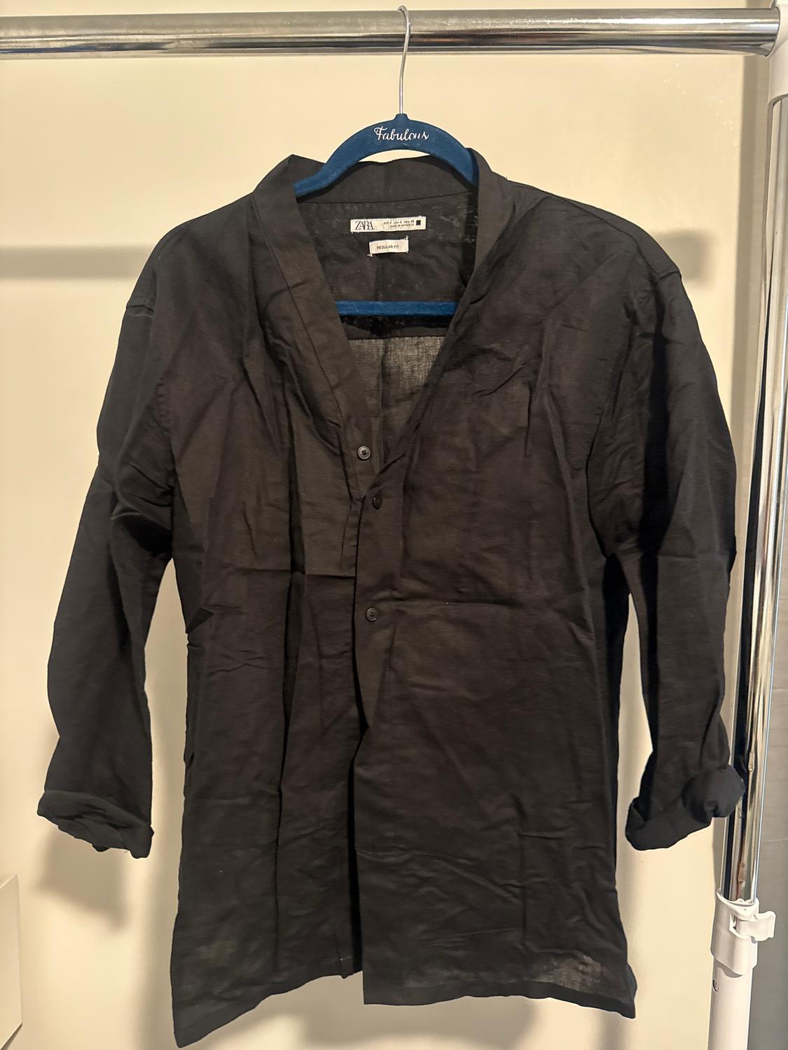 Black long-sleeved shirt hanging on a blue hanger with the word "Fabulous". White background and visible metal rail.
