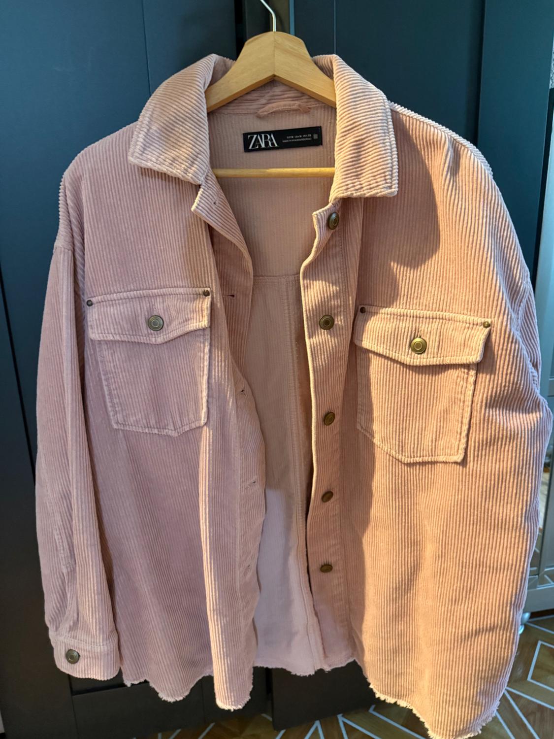 Light pink corduroy jacket hanging on a wooden hanger. Visible tag: "ZARA". Dark background.