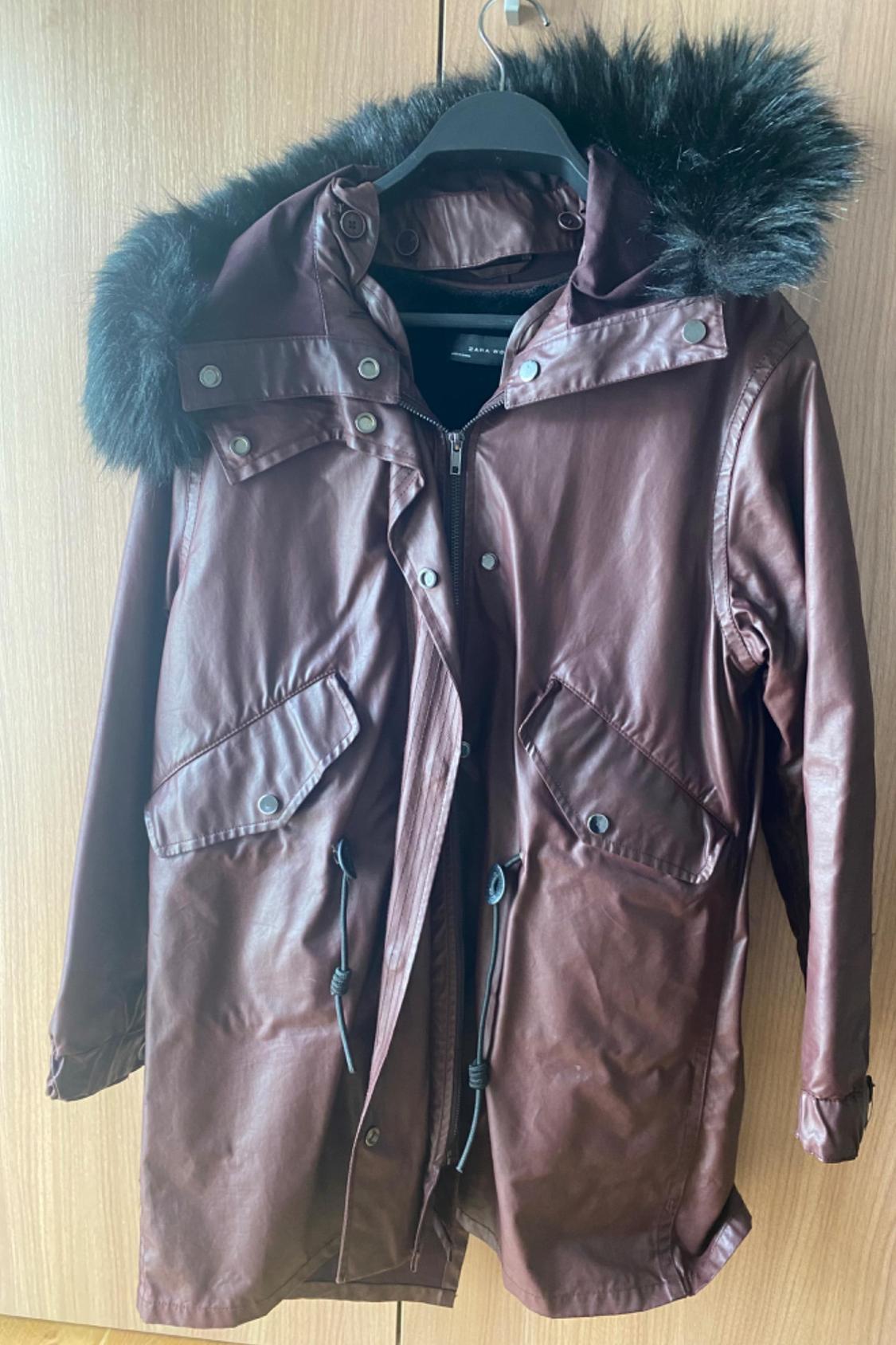 Front view of a brown coat with a black fur hood and front flap pockets.