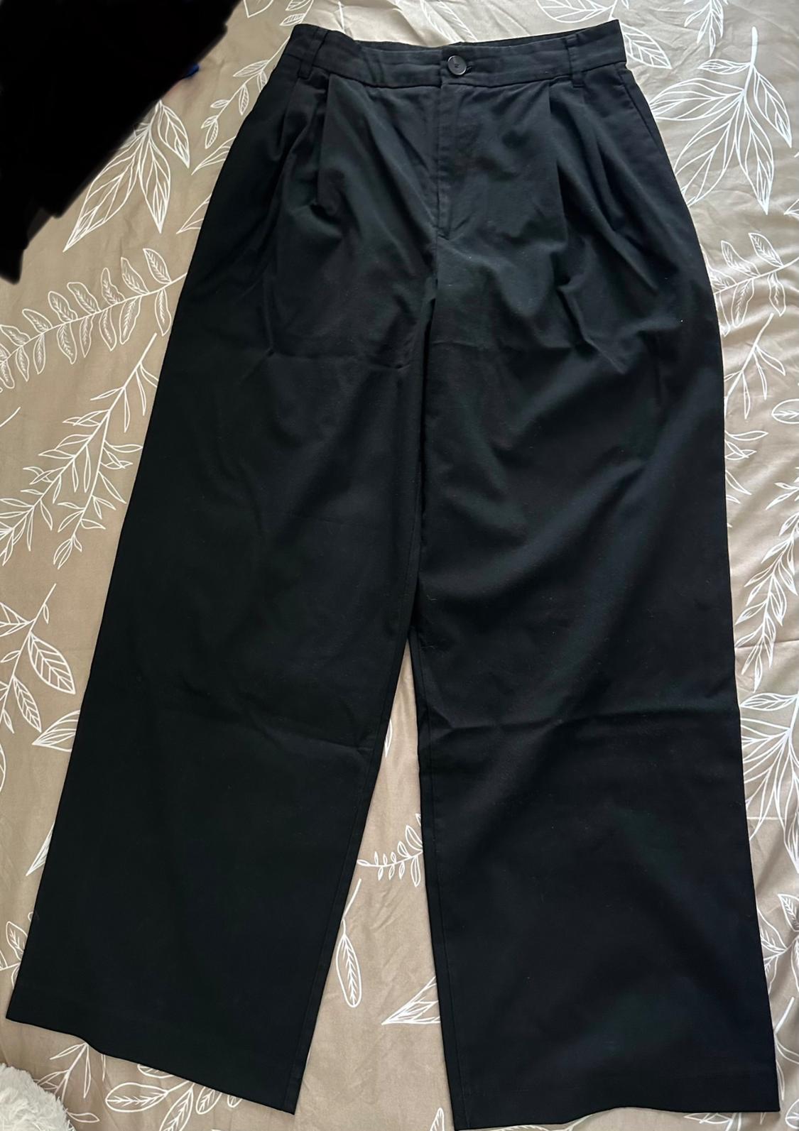 Black wide-leg trousers on a bed with a white leaf-patterned duvet.