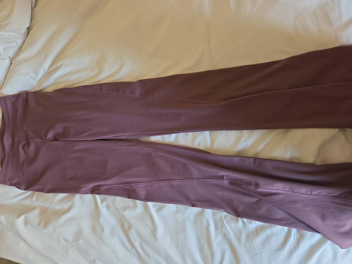 Dark pink long trousers laid out on a bed with white sheets.