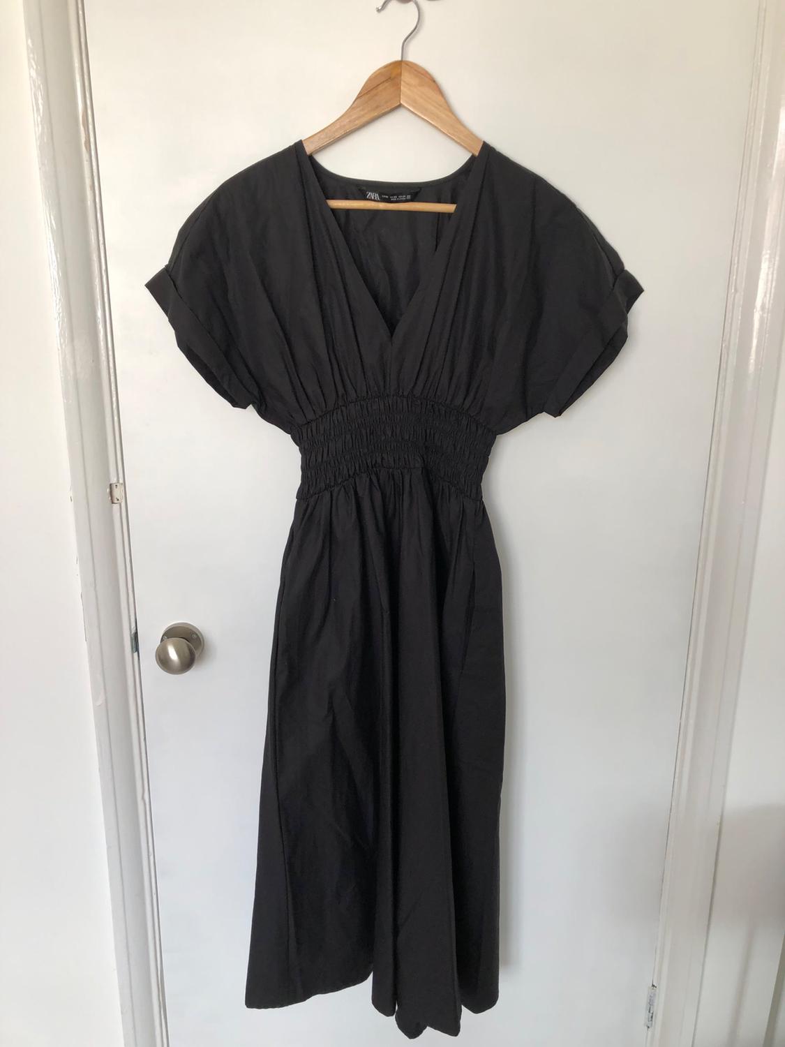 Front view of black dress with short sleeves and gathered waist hanging on a hanger.
