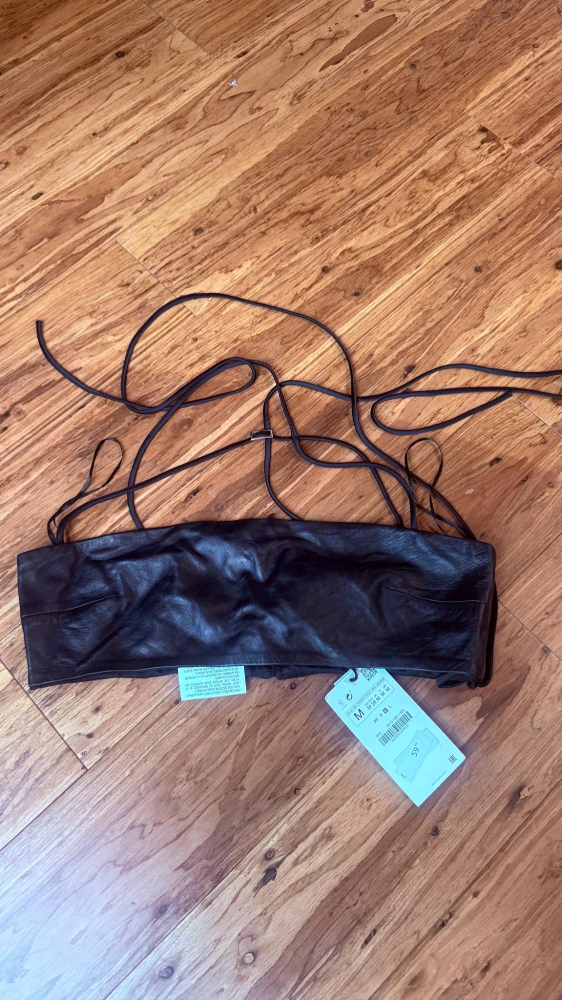 Faux leather black top with long straps on a wooden floor. Label with the text M, XS S M L and 59.