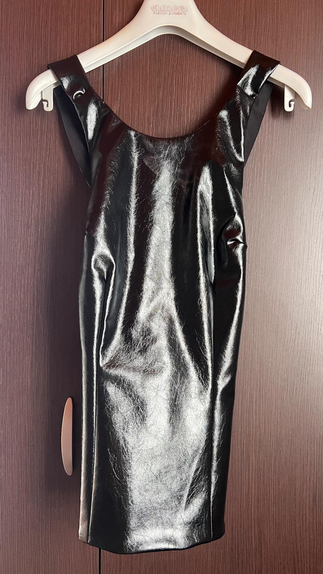 Shiny black dress hanging on a white hanger with the brand "GUARDAROBA" in a dark wooden wardrobe.