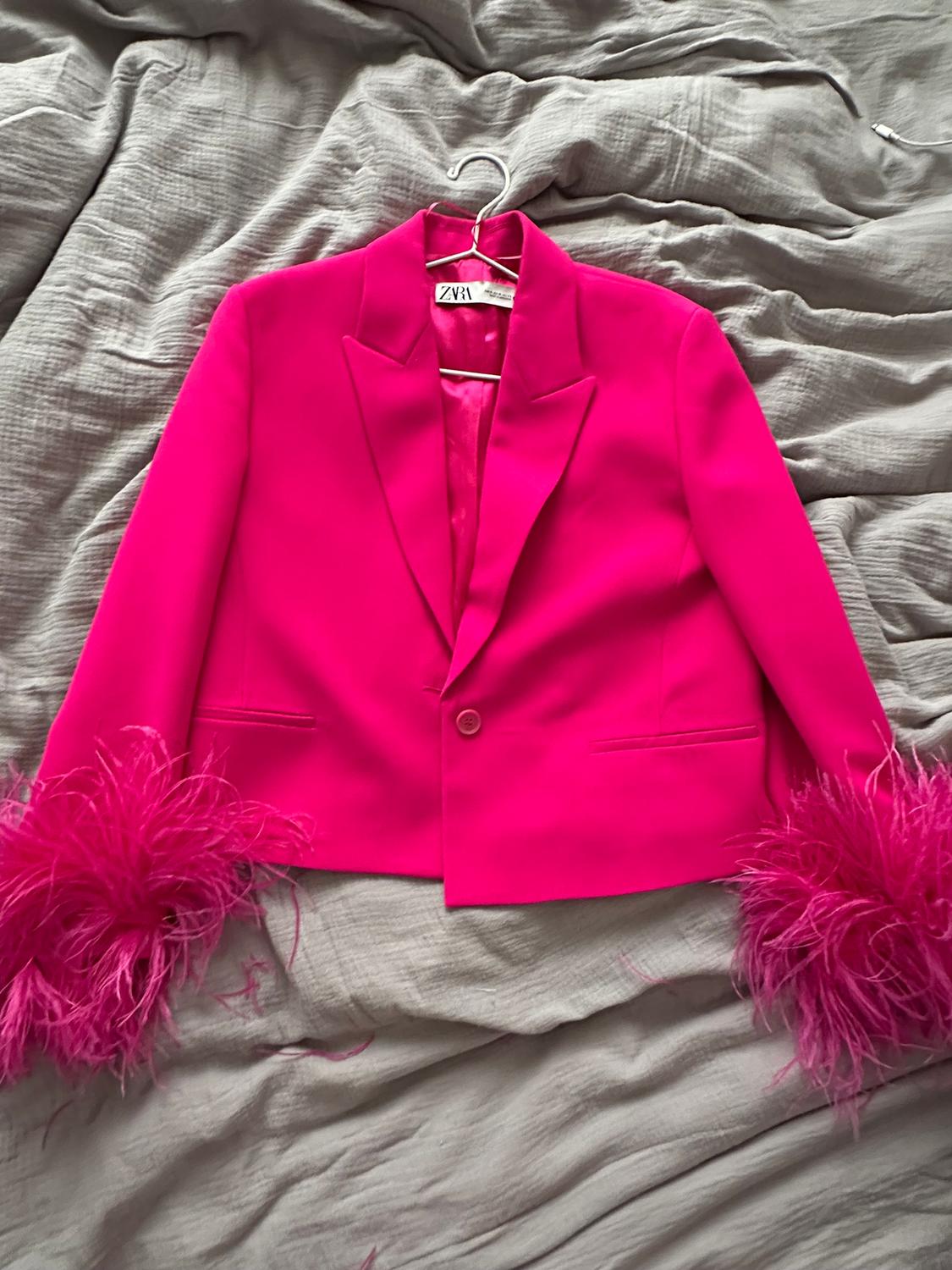 Fuchsia jacket with feathers on the cuffs on a grey bed. Visible label with text "ZARA".