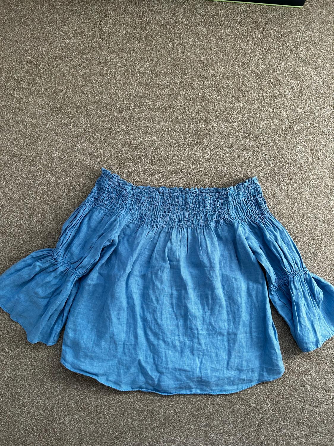 Off-the-shoulder blue blouse with long, flared sleeves, on a beige rug.
