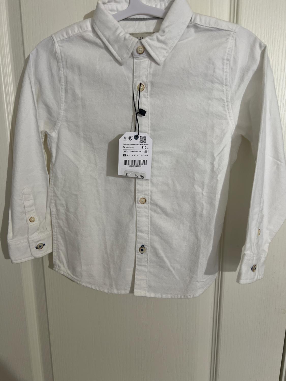 White long-sleeved shirt hanging on a hanger over a white door. Visible tag with text: 5 YEARS 110 cm $ 19.90.