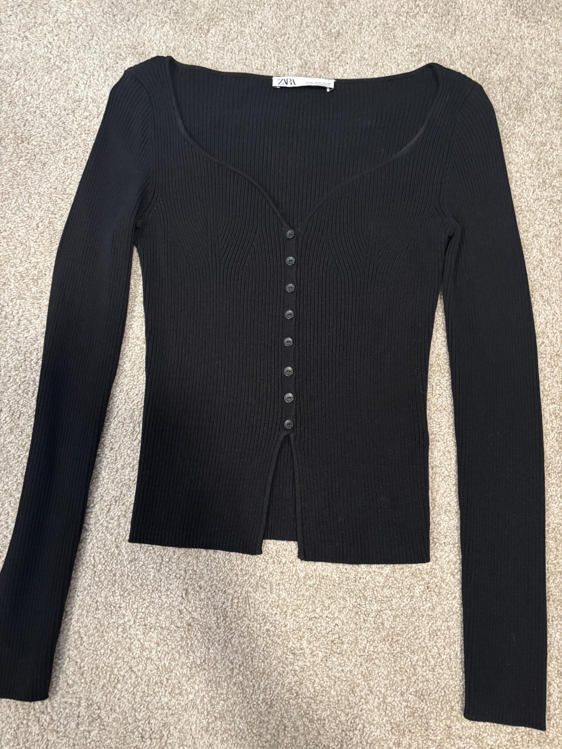 Black long-sleeve cardigan with front buttons on beige carpet. Visible tag on the collar.