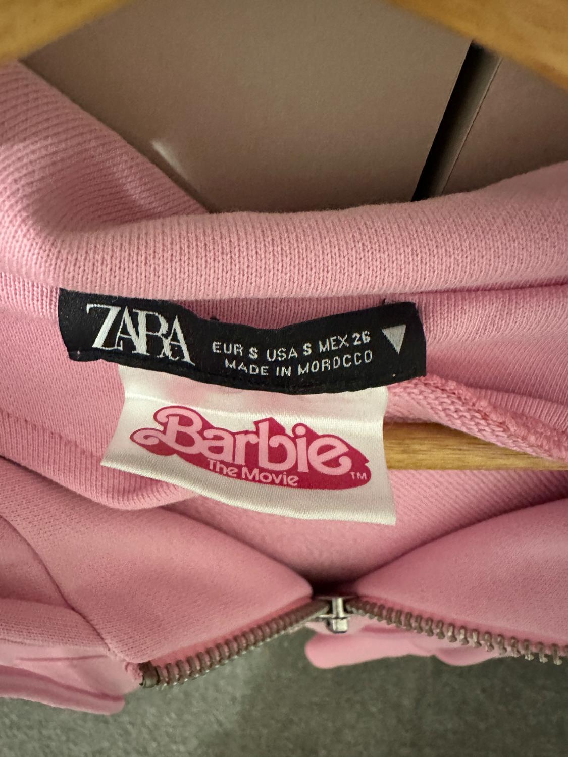 Pink sweatshirt label with text "ZARA EUR S USA S MEX 26 MADE IN MOROCCO" and "Barbie The Movie" in pink lettering on a white background.