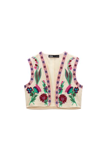 Front view of a beige waistcoat with colourful floral embroidery on the chest and decorative trim.