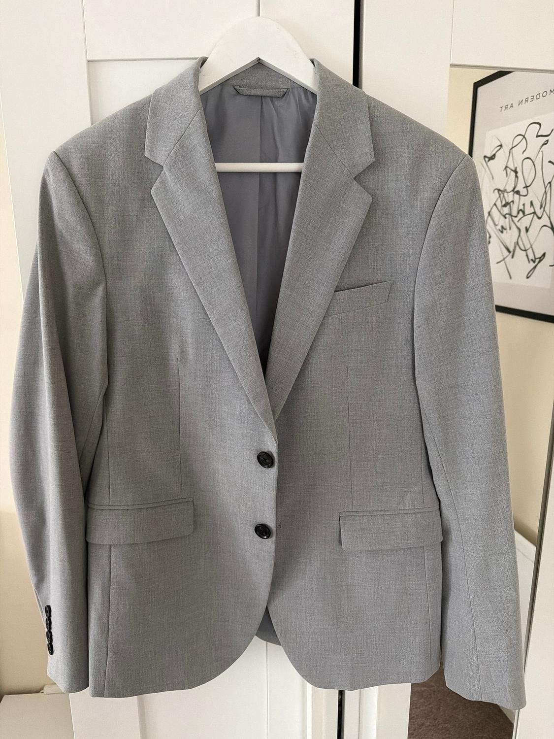 Light grey jacket hanging on a white hanger in front of a wardrobe. Background with a black and white modern art painting.