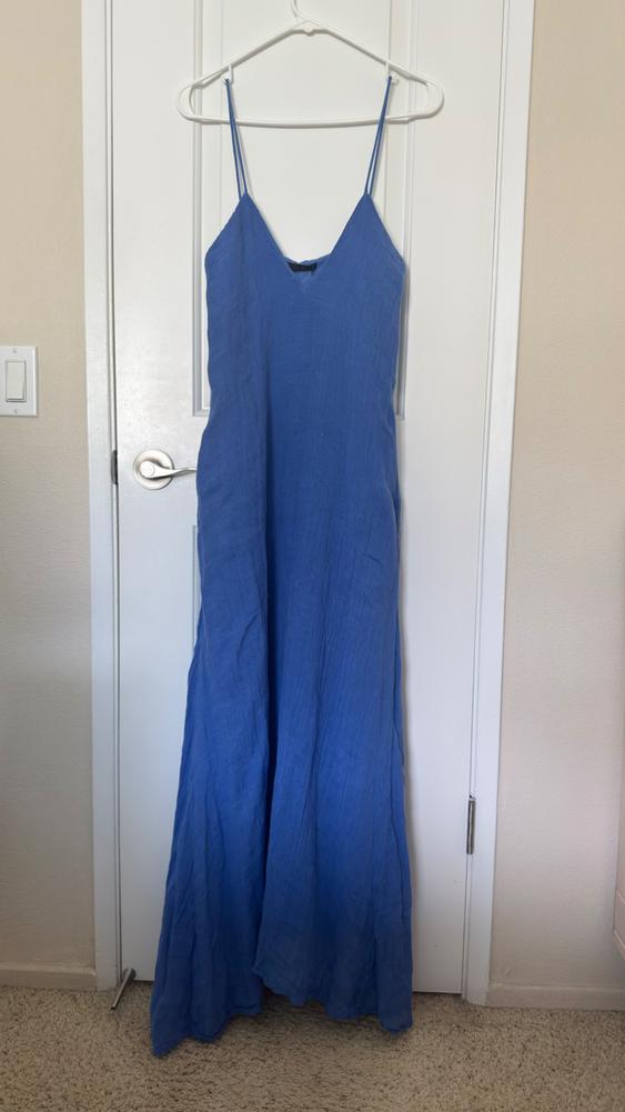Blue spaghetti strap dress hanging on a white hanger over a white door. Beige wall background and light-colored rug.