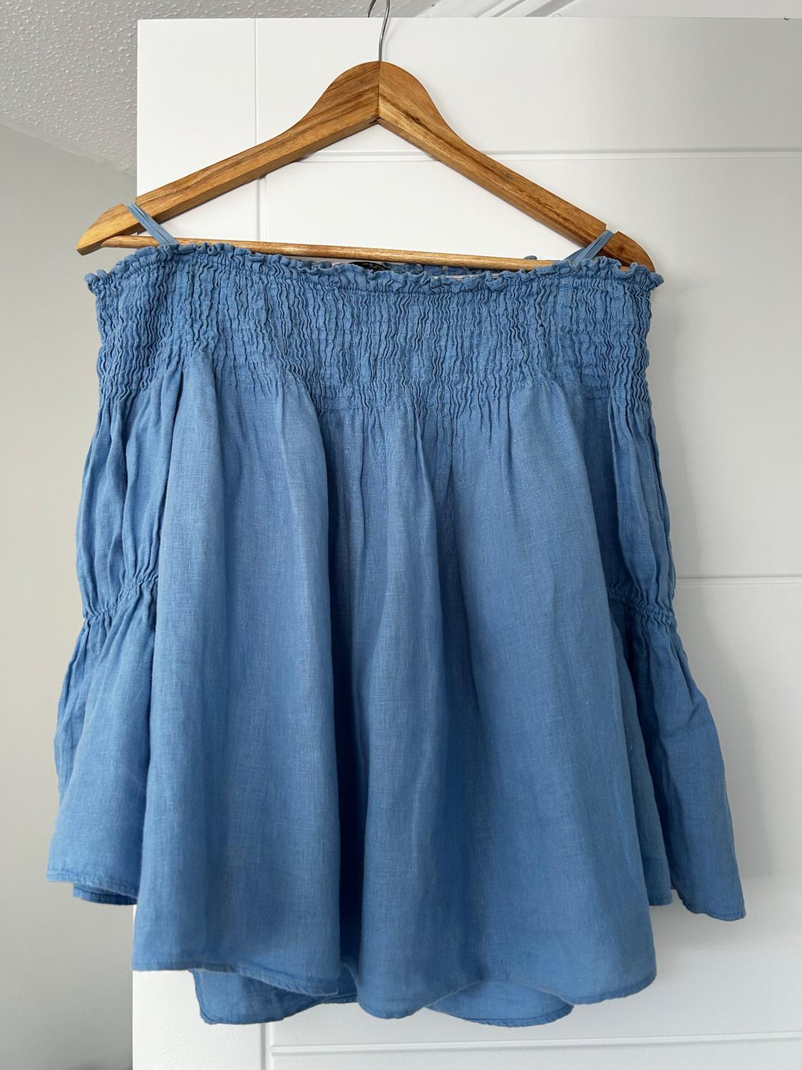 Blue camisole top with ruching across the bust, hanging on a wooden hanger against a white background.
