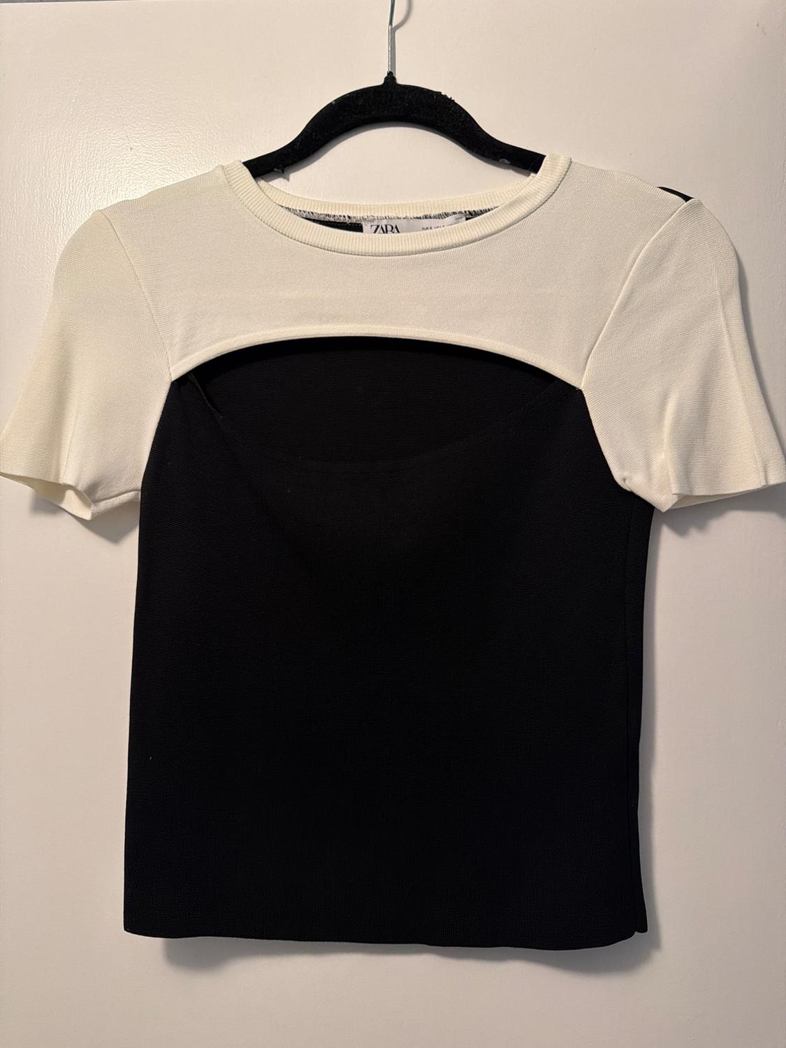 Two-tone T-shirt hanging on a black hanger. The top part is white and the bottom part is black. The label is visible on the collar.