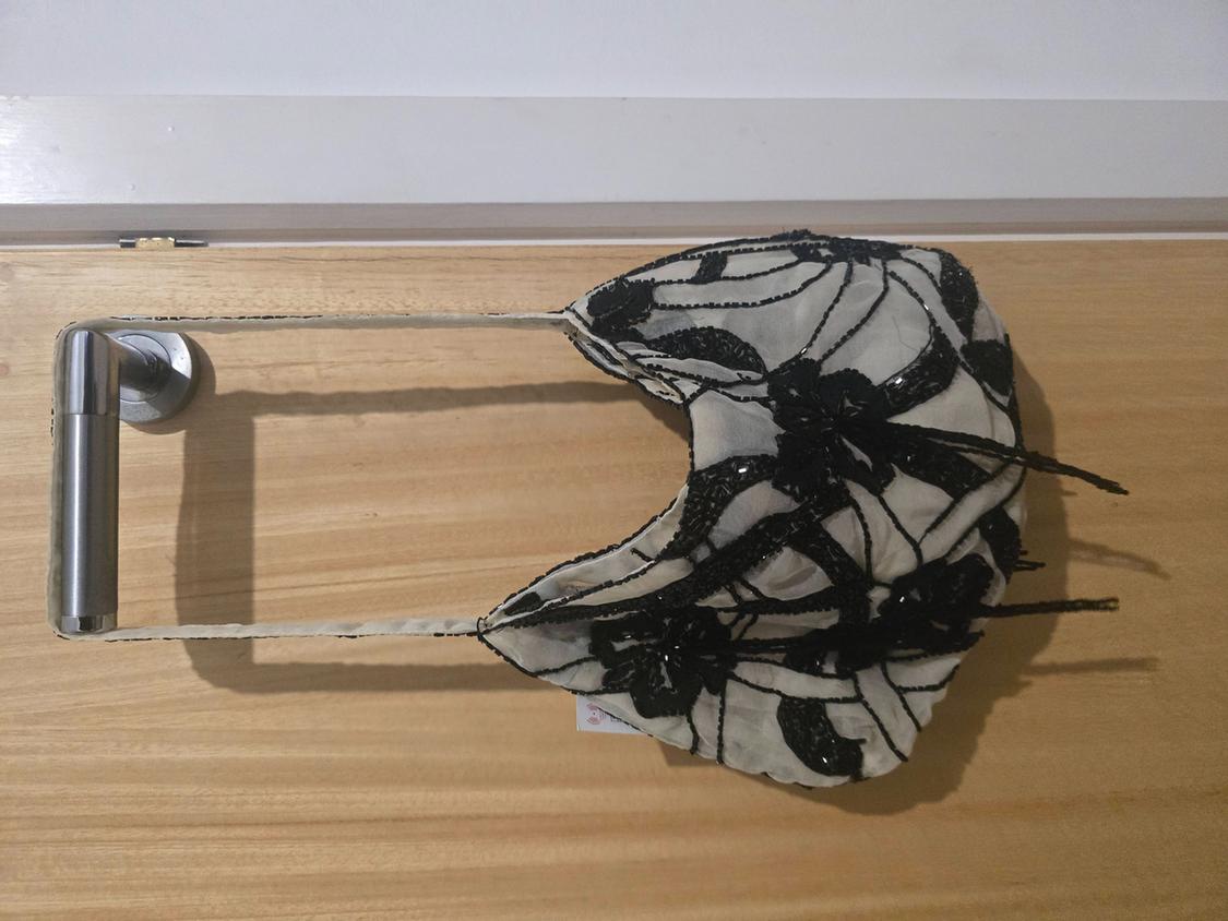 Handbag hanging on a wooden door handle. The handbag is white with black floral and leaf embroidery.