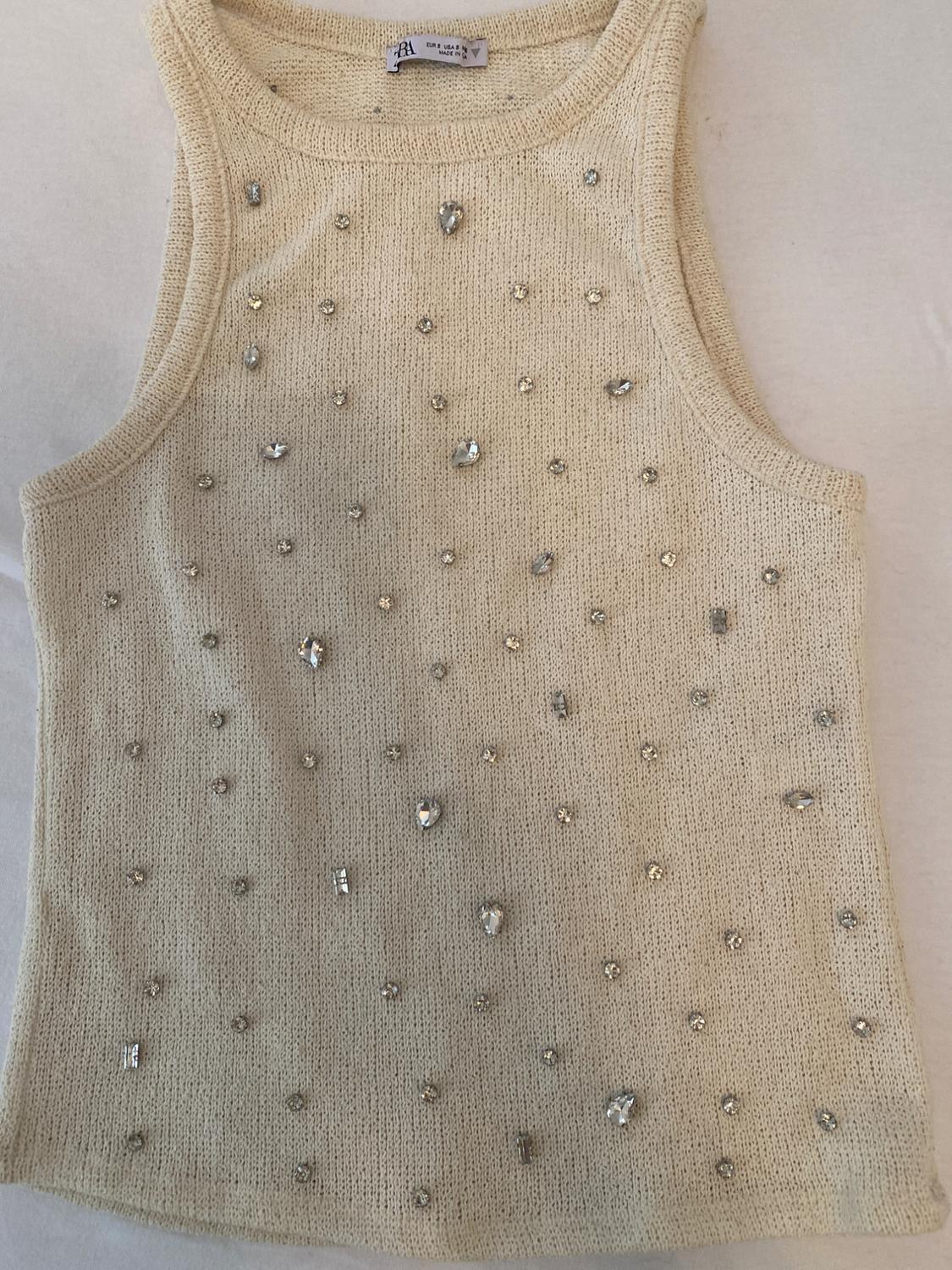 Cream sleeveless knit top with rhinestone details. ZARA label visible on the neck. Garment laid flat on a light background.