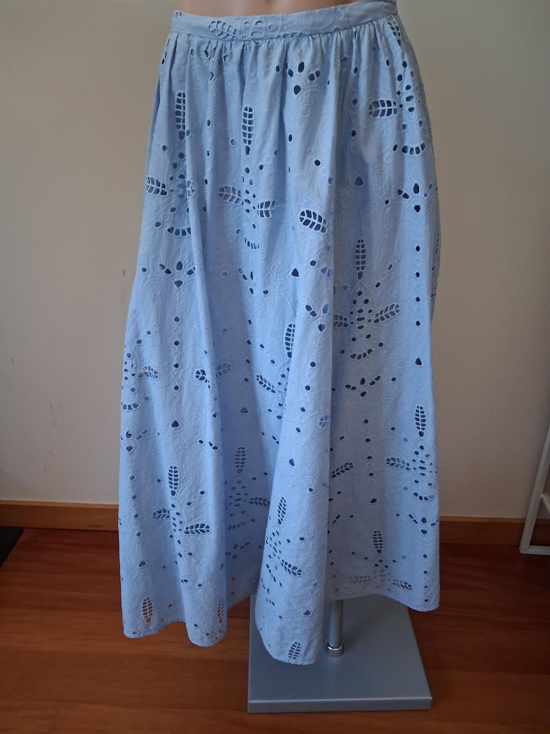 Light blue skirt with floral cut-out design on a mannequin on a wooden floor. Indoor setting with a white background.