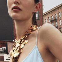 Image 1: Woman in a light blue dress and large gold necklace, standing in an urban setting with brick buildings in the background.