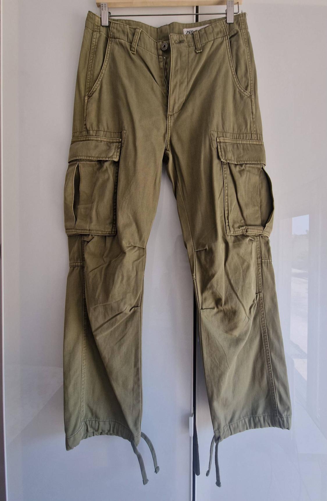 Olive green cargo trousers hanging on a hanger against a white background. They feature side pockets, drawstrings at the hem and a label with the text ZARA.