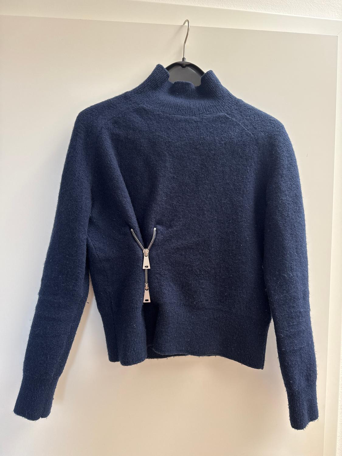Dark blue high-neck jumper with a zip at the back, hanging on a hanger against a white background.