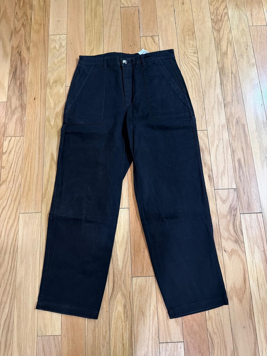 Straight-cut black pants with front pockets, placed on a light wooden floor.