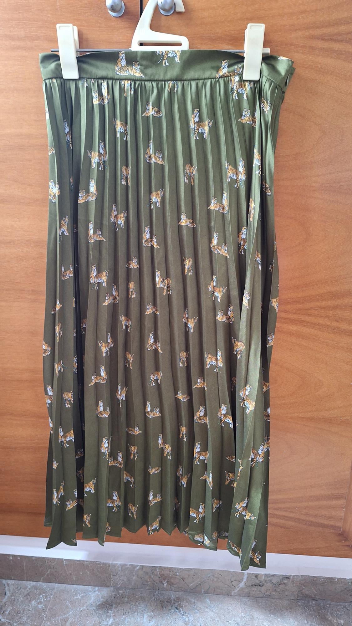 Green pleated skirt with tiger print, hanging on a white hanger against a wooden background.
